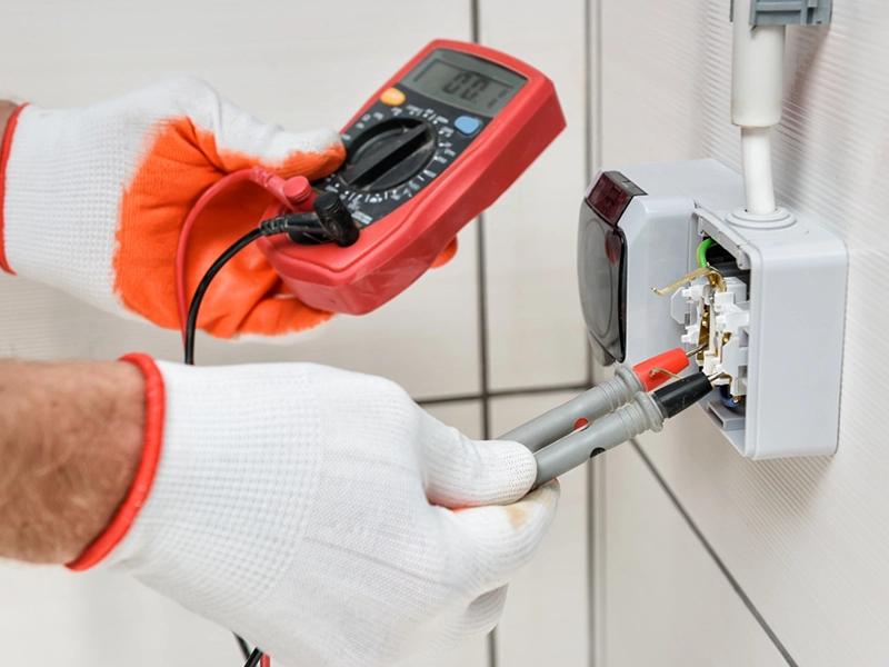 manos midiendo con voltímetro en enchufe de luz